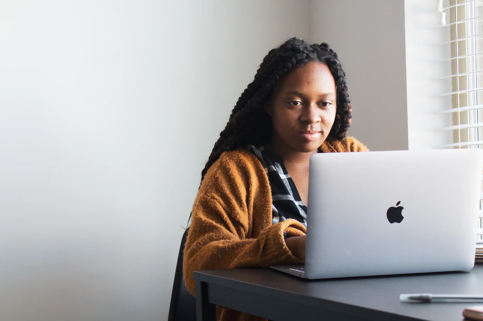 A woman working on a laptop at a desk by a bright window