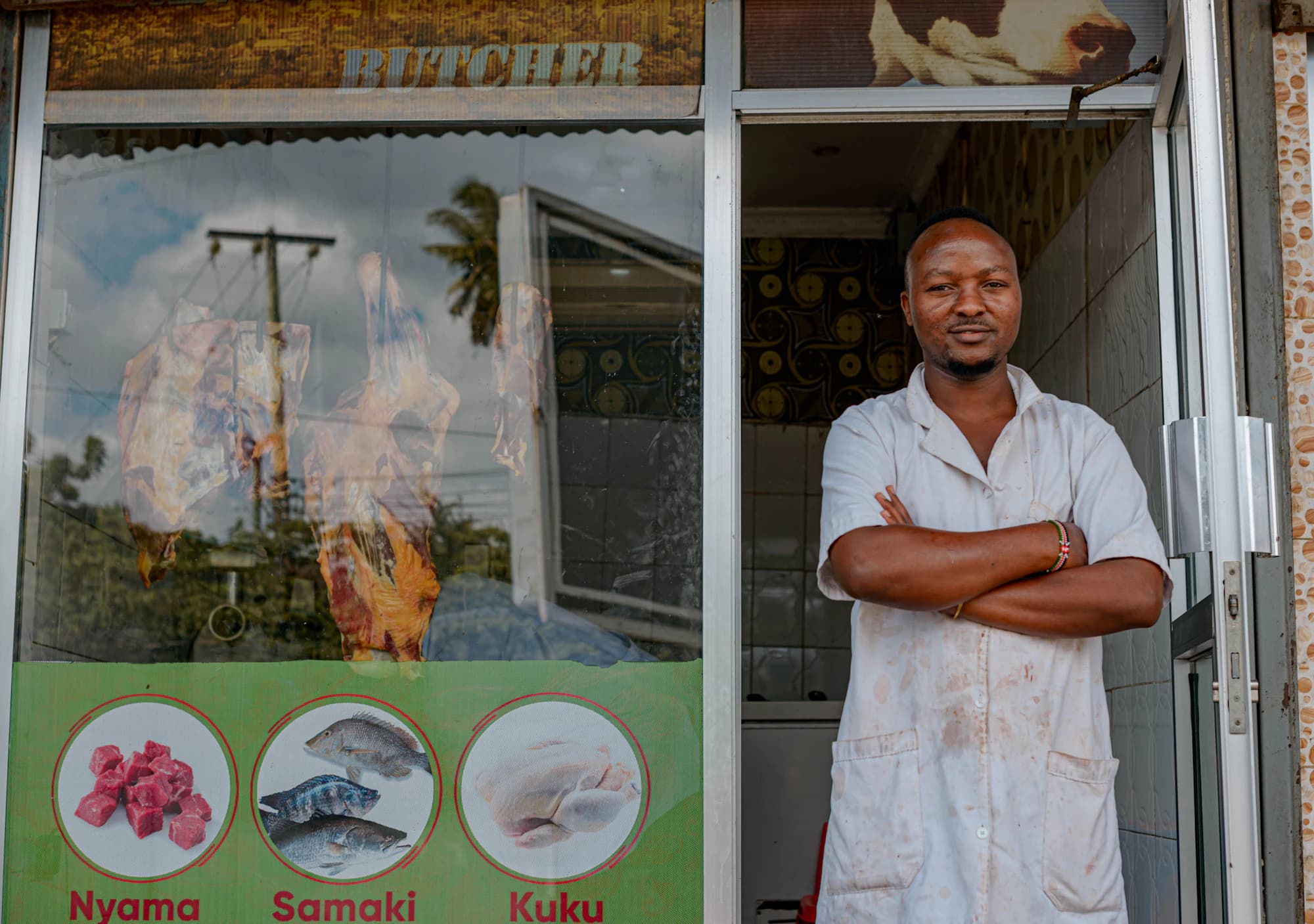A shop owner standing with arms crossed in the doorway of his butcher shop